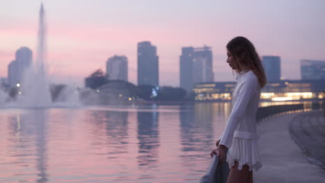 woman enjoying a sunset view of a city lake with fountains and skyline