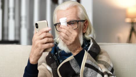 sick old man sitting on sofa and showing pills while videochatting on smartphone