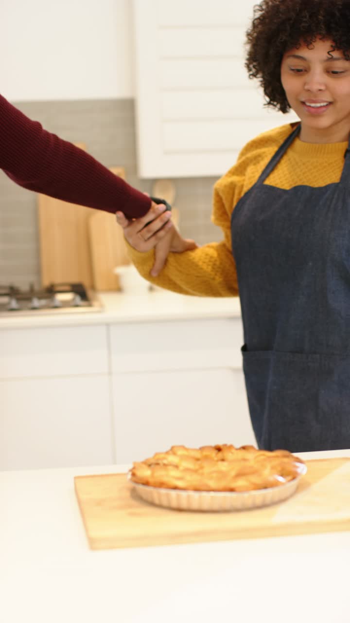 Video verticale: coppia di etnie diverse che si abbraccia in cucina, l'uomo guida la donna verso una crostata per ammirarla