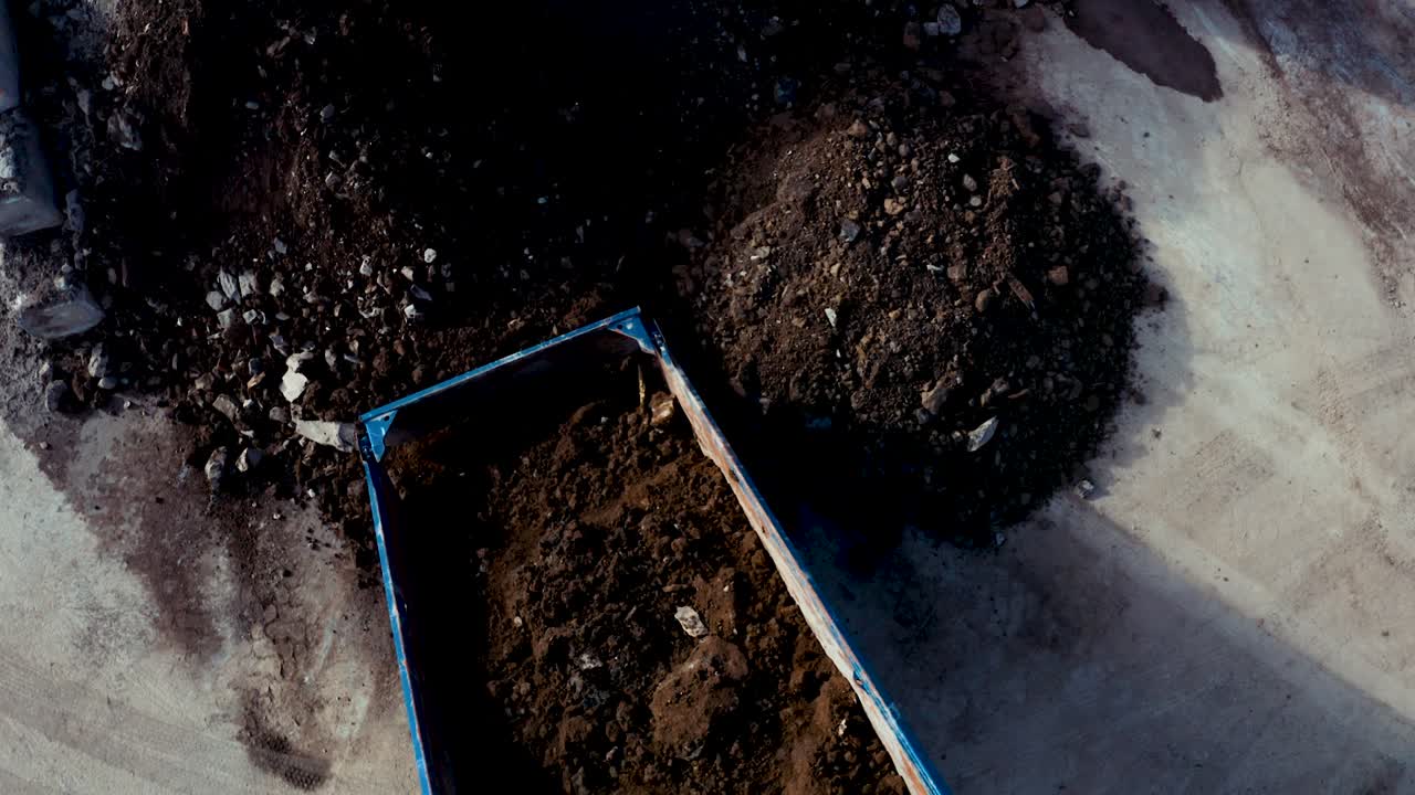 Vista aerea dall'alto di un dumper che scarica rocce e terra in un mucchio. Ripresa da drone con leggero movimento di pan in basso