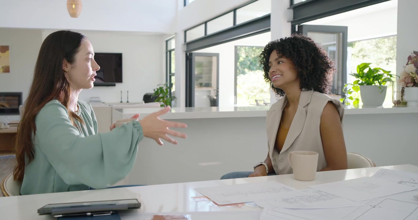 Diverse female colleagues with left woman holding mug presenting design plans to decide at home