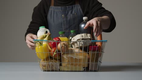 studio shot of shop worker checking basic food items in supermarket wire shopping basket