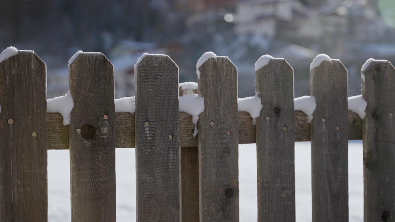 Cold winter outdoor in small town or farm in Europe snow falls on wooden fence. Sunny morning in cold freezing day. Snow storm at night falling on local village or ski resort town. Barrier with snow