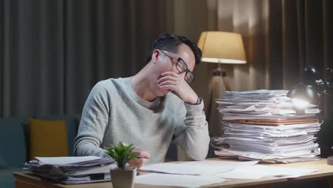 tired asian man yawning while working hard with documents at home