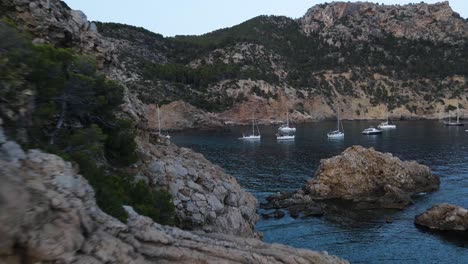 Drone-view-of-sailboats-docked-along-seaside-in-Cala-d'egos-beach,-Spain