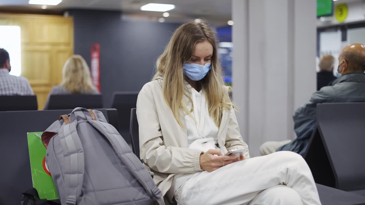 mujer turista con máscara de protección médica usando teléfono móvil en el aeropuerto