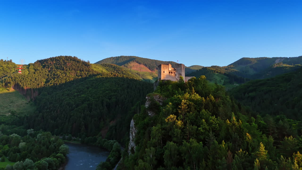 Castle towers over lush valley. A historic castle stands atop a green hill, surrounded by dense forests and a flowing river under a clear blue sky