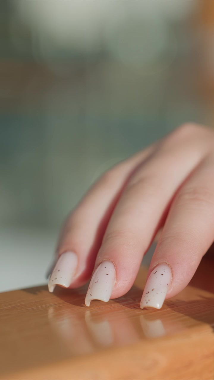 Close up of hand with long pointed nails. Focus remains consistently on texture details like nail polish. Soft natural light creates subtle reflections enhancing wood grain