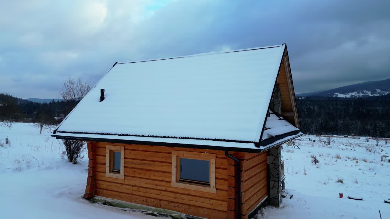 Una casa di montagna in legno circondata da neve alta, ripresa con un movimento fluido di rotazione della camera. Tranquilla ambientazione alpina con dettagli ghiacciati e bellezza naturale invernale.