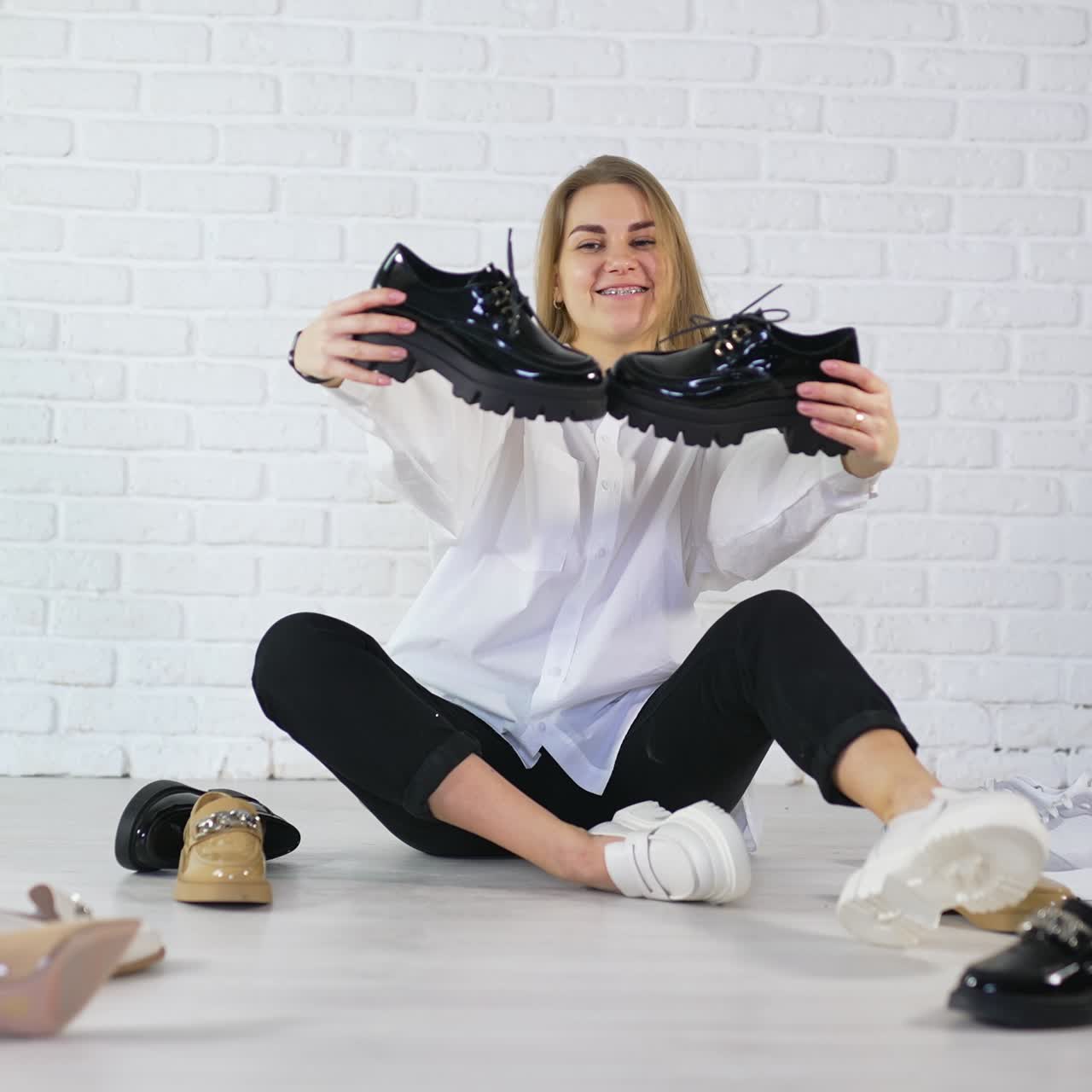 Giovane donna con capelli lunghi che mostra nuove scarpe nere lucide con lacci. Donna tra le calzature su sfondo bianco