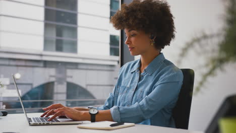 businesswoman in modern office working on laptop and making notes in notebook