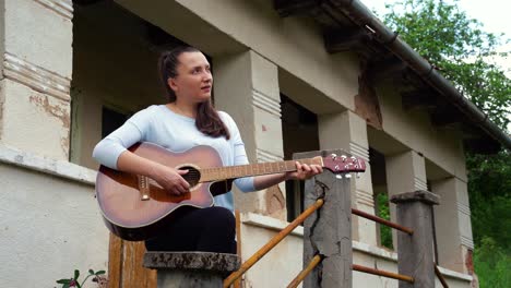 a young woman plays the guitar near an old house