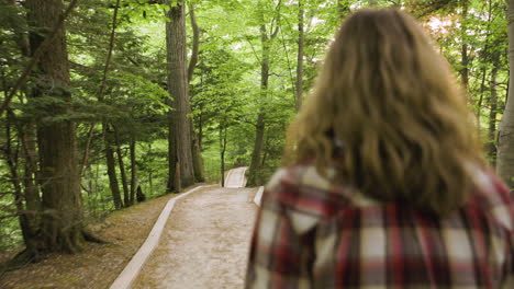 handheld shot following a young woman walking through the woods at sunset