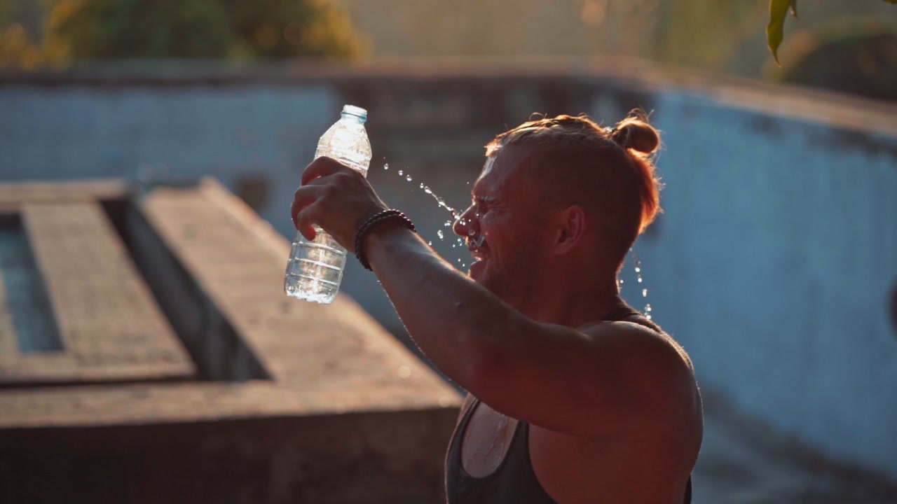 Uomo atletico che si rinfresca con acqua dopo l'allenamento al tramonto