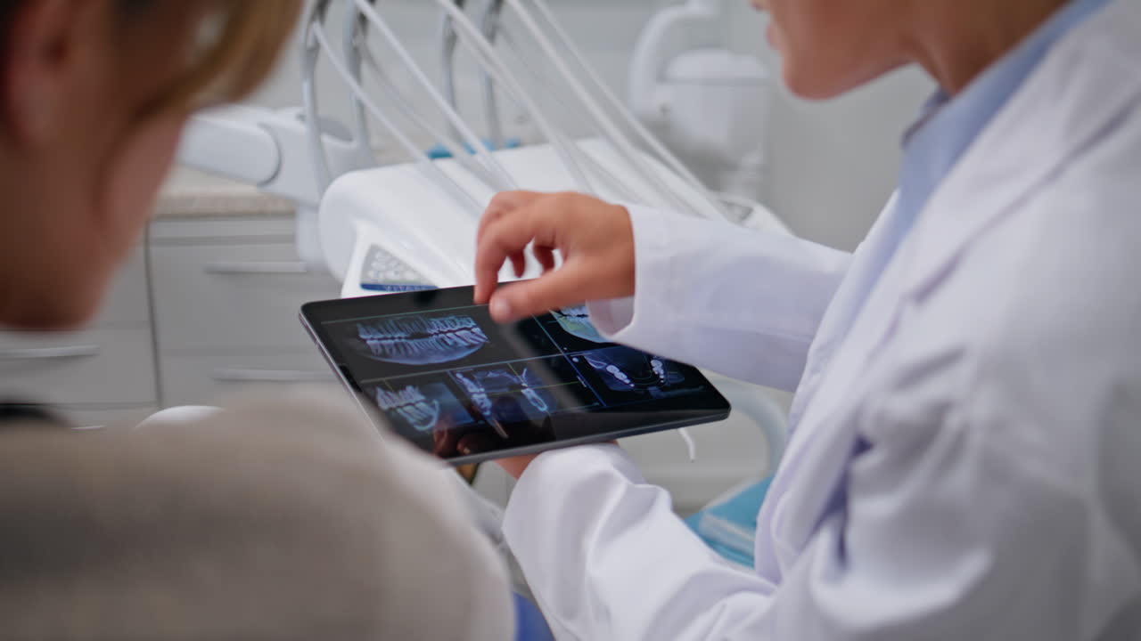 Dentist showing dental x-rays on tablet at stomatology consultation closeup