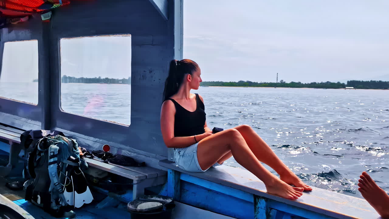 Dark-haired woman relaxes on a dive boat, admiring the wavy sea off Gili Trawangan's coast