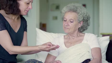 hija sentada en la cama de la madre, dándole pastillas