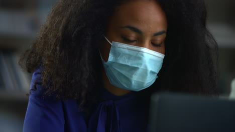 african american businesswoman wearing mask searching laptop computer in office.