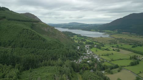 Flying-over-from-forested-mountainside-to-flat-patchwork-field-farmland-with-Bassenthwaite-Lake-in-distance
