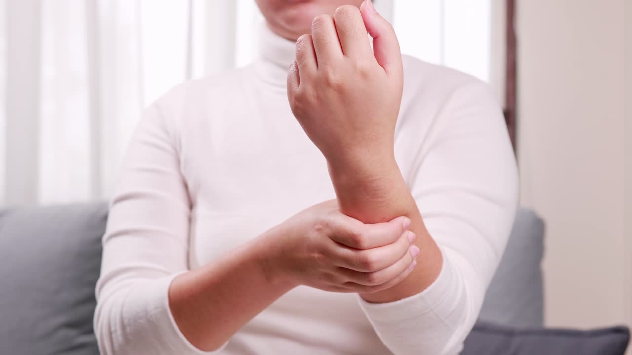 A woman in a white shirt sits on the sofa and is massaging her wrists