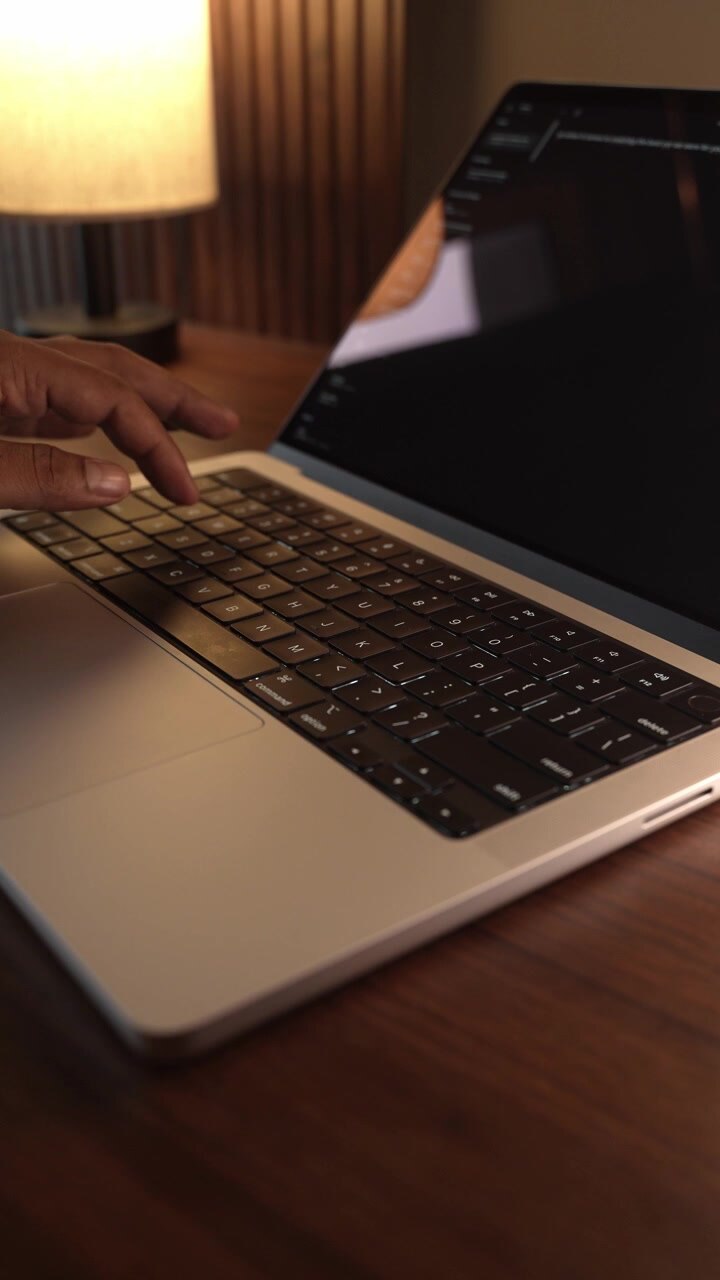 Hænder der taster på laptop-tastatur i et varmt, hyggeligt oplyst rum.