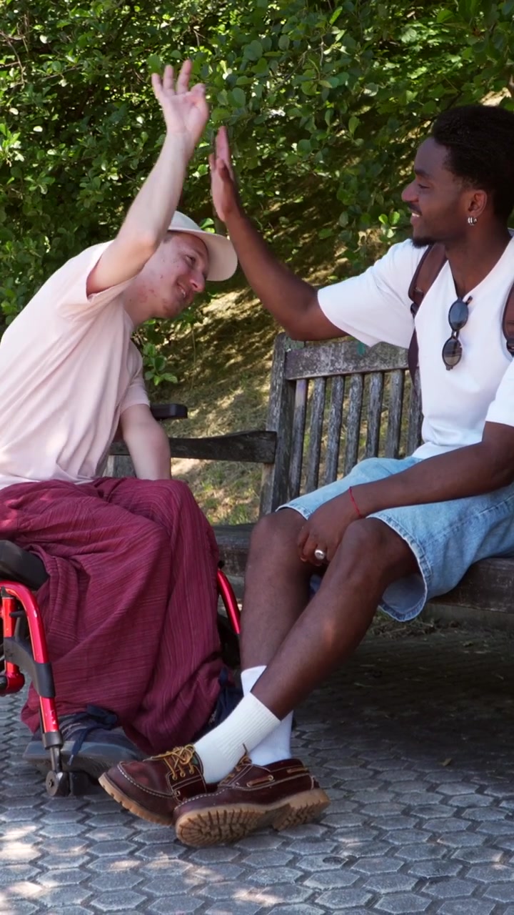 Two Young Men Talking and High-Fiving on a Park Bench
