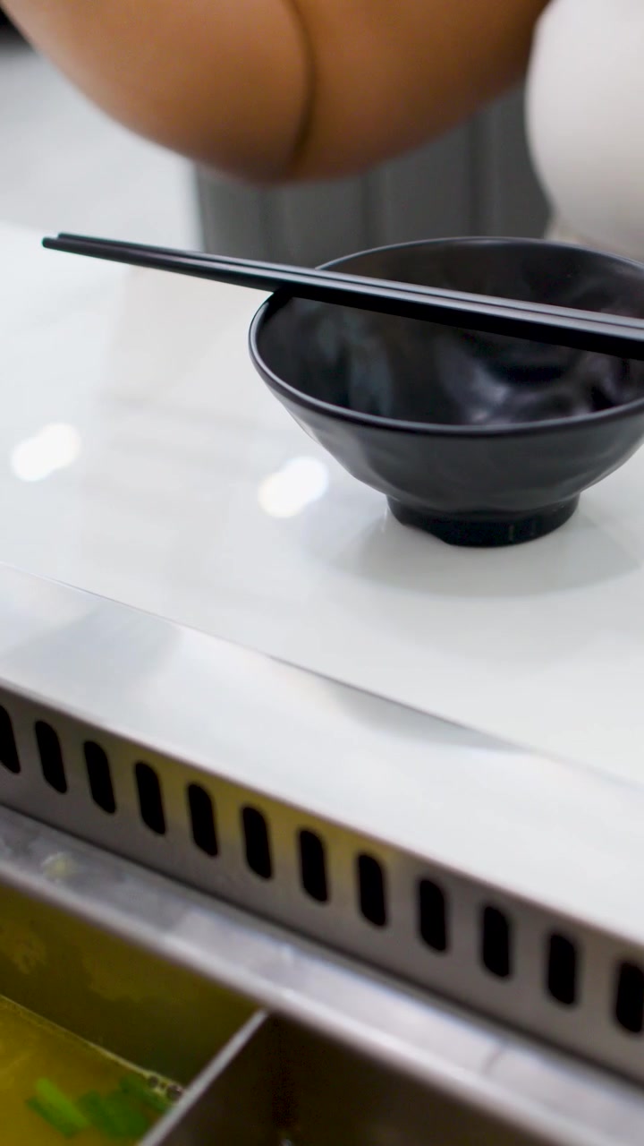 Close-up of hands arranging a bowl and chopsticks beside a simmering Asian hot pot station