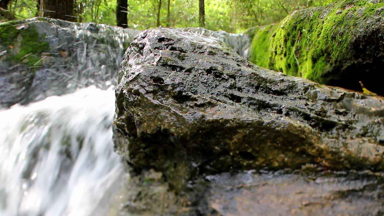 Sped up waterfall, wide angle close up view of a large wet rock