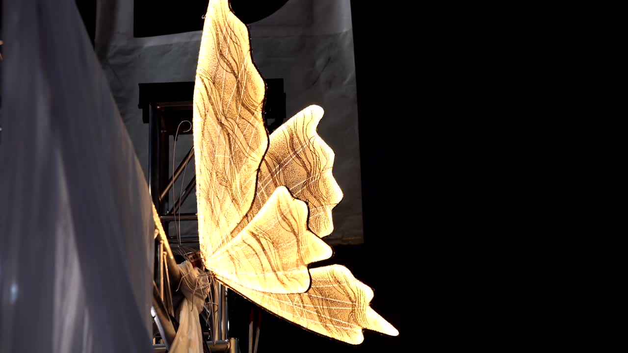 large illuminated golden wings on dark stage backdrop during theatrical performance