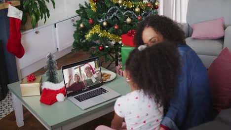 Happy-african-american-mother-and-daughter-on-video-call-with-male-friend-and-son-at-christmas-time