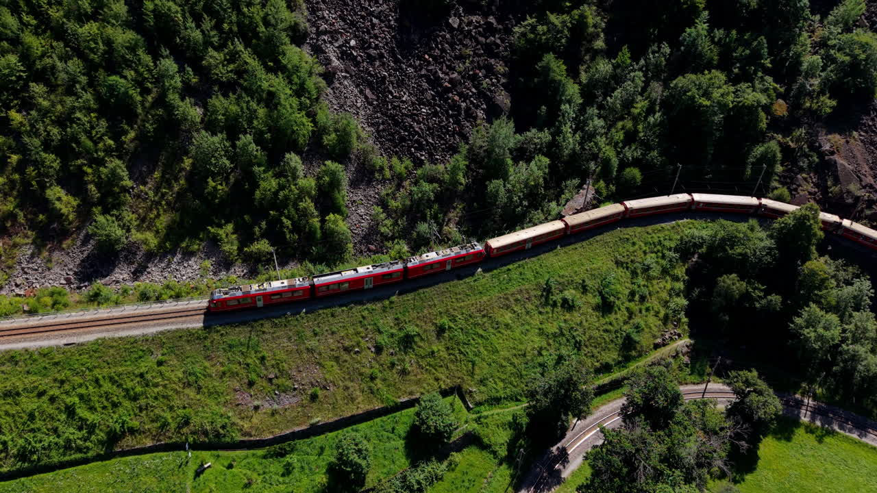 Aerial of red Bernina train in green Swiss landscape, peaceful travel
