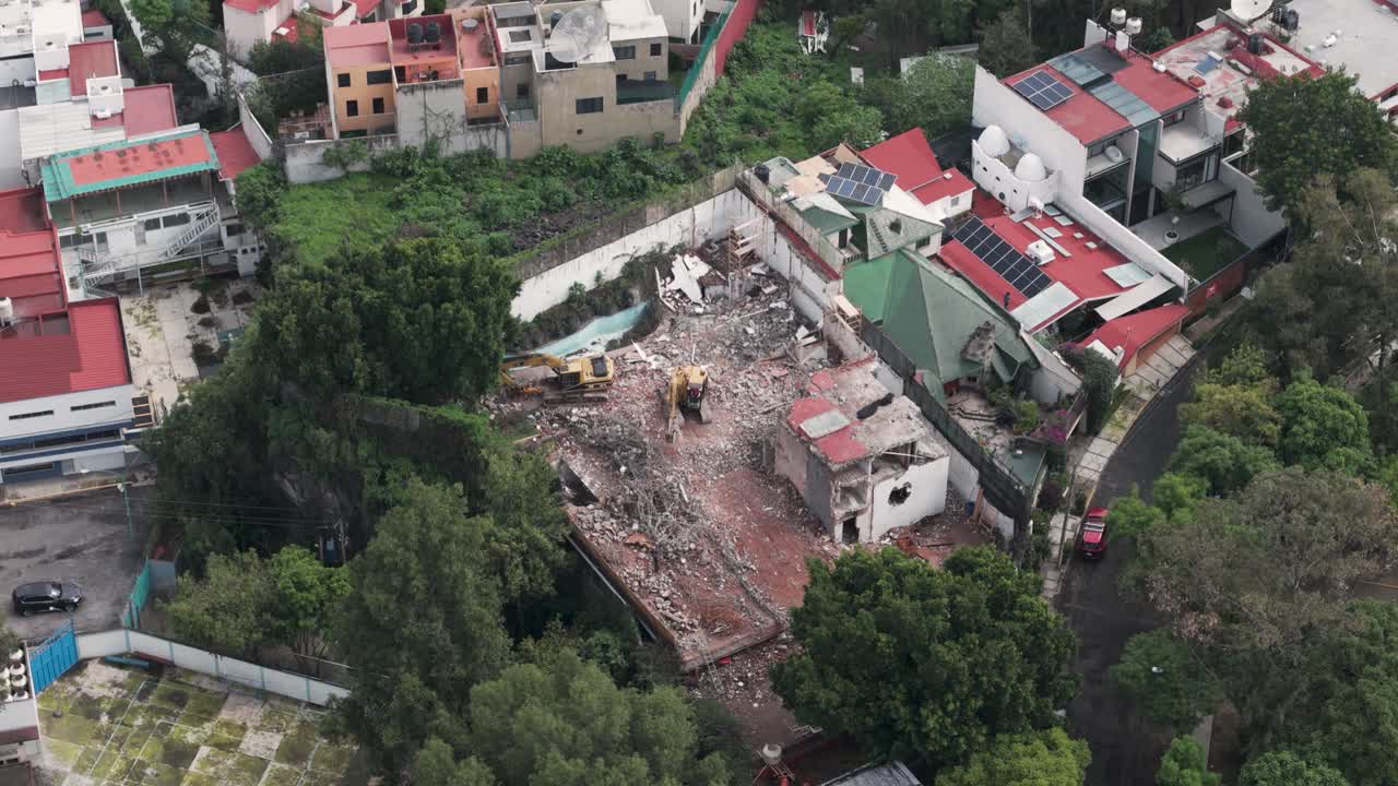 Slow-motion aerial video of a backhoe clearing debris from a demolished house