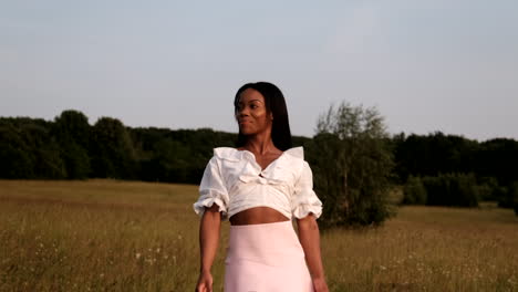 une femme noire heureuse se promène dans le champ d'été au coucher du soleil en profitant du temps chaud.