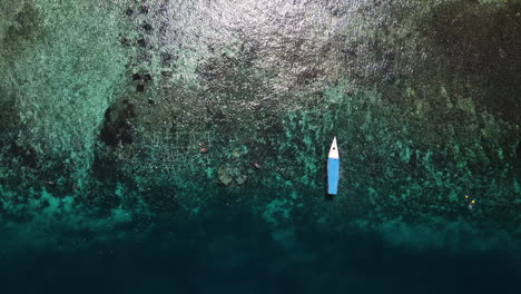 Barco-Turístico-Flotando-En-Agua-Azul-Clara-Con-Arrecifes-De-Coral-En-El-Suelo-Del-Océano-En-Bali,-Indonesia