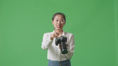 화가 난 아시아인 사진작가는 카메라에서 사진을 보고 스튜디오에서 녹색 스크린 배경에 서서 누군가에게 소리를 질렀다.