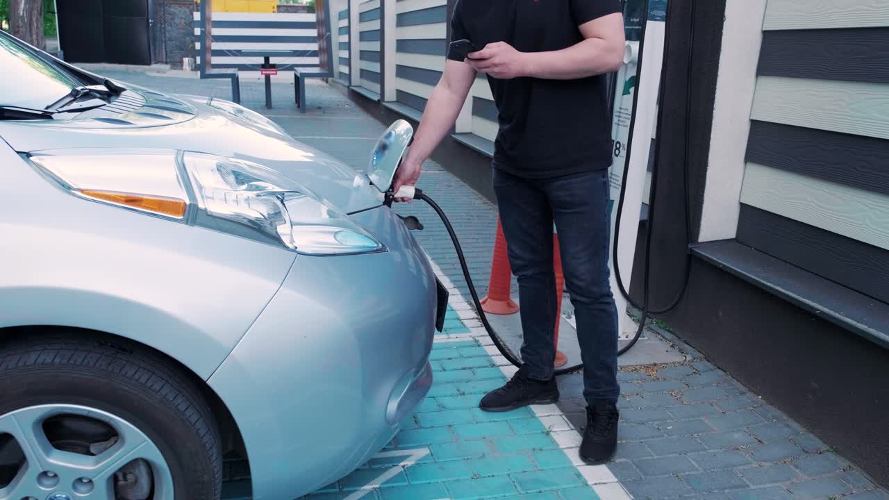 전기 자동차의 연료 충전 과정: 전기 에코 자동차가 충전하는 치 아래의. 전기 자동차 충전 치는 자동으로 열립니다. 남성 손이 발기 된 자동차를 입합니다.