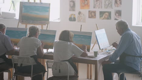 a young female art teacher demonstrates the technique of painting with acrylic paints on canvas for a group of retirees. group of senior men and women