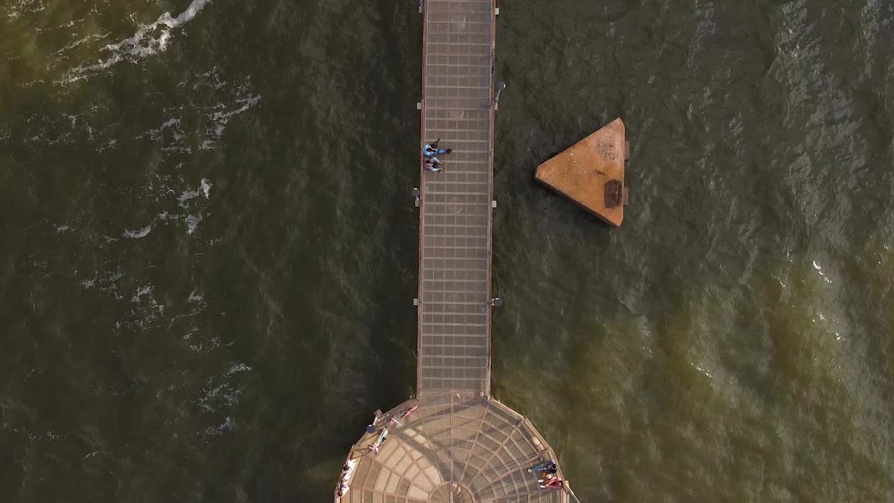 muelle metálico en el agua con turistas de pie en él mientras observan las olas