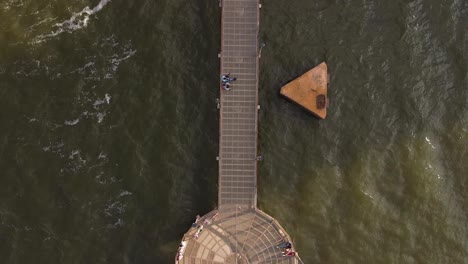 Metal-pier-on-the-water-with-tourists-standing-on-it-while-watching-the-waves