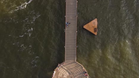 metal pier on the water with tourists standing on it while watching the waves