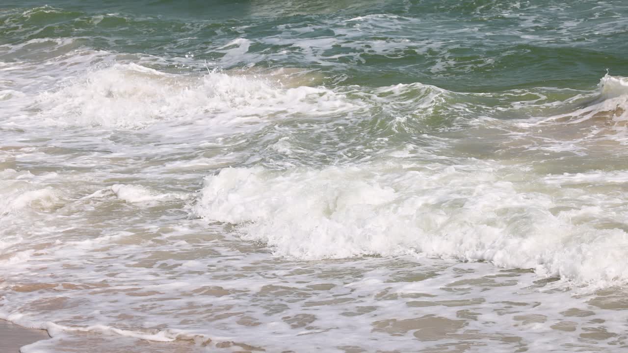 파도가 모래 해변에 리적으로 부히고 있습니다.