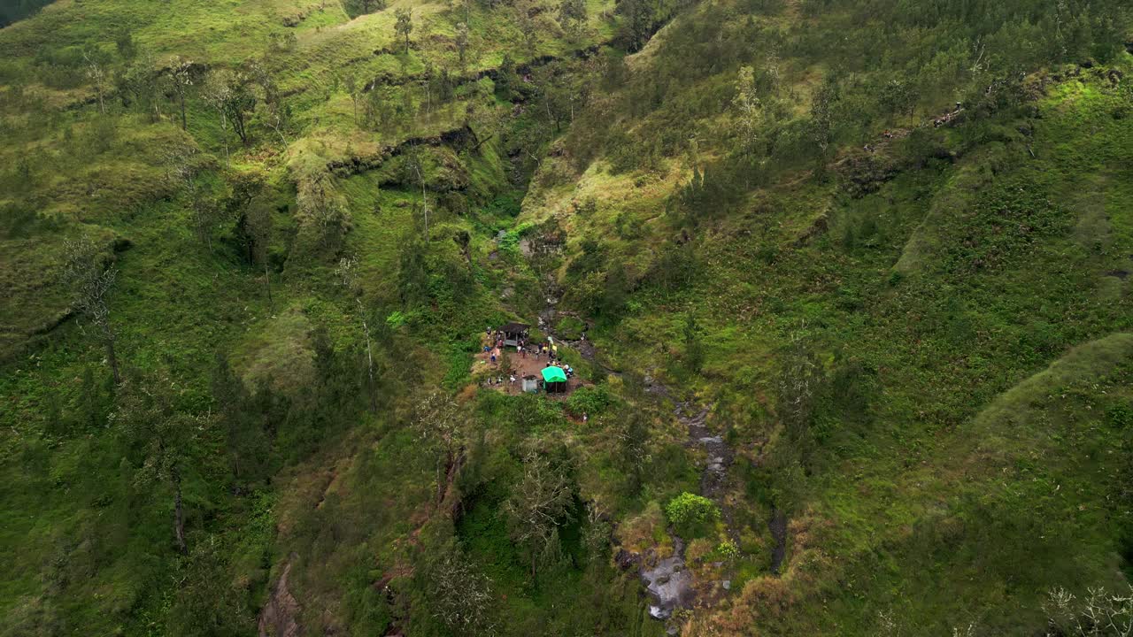 On the journey to the summit, people take a break at a peaceful campsite set on a vibrant green mountain slope offering scenic views and fresh air in the highlands.