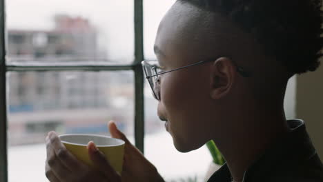 Elegante-Joven-Afroamericana-Estudiante-Tomando-Café-En-Casa-Mirando-Por-La-Ventana-Pensando-En-Planificar-Con-Anticipación-Disfrutando-De-Un-Estilo-De-Vida-Relajante-Usando-Gafas-De-Moda