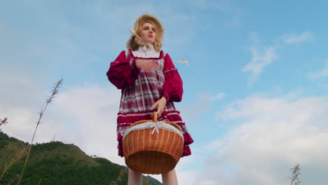 modelo de mujer rubia en vestido tradicional de renacimiento medieval de ángulo bajo sosteniendo cesta de comida