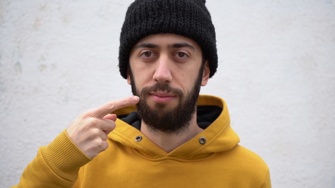 joven barbudo apuntándose con el dedo a la boca