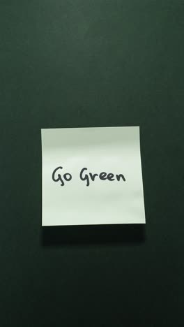 hands posting go green sticky note on dark green wall, showcasing eco awareness