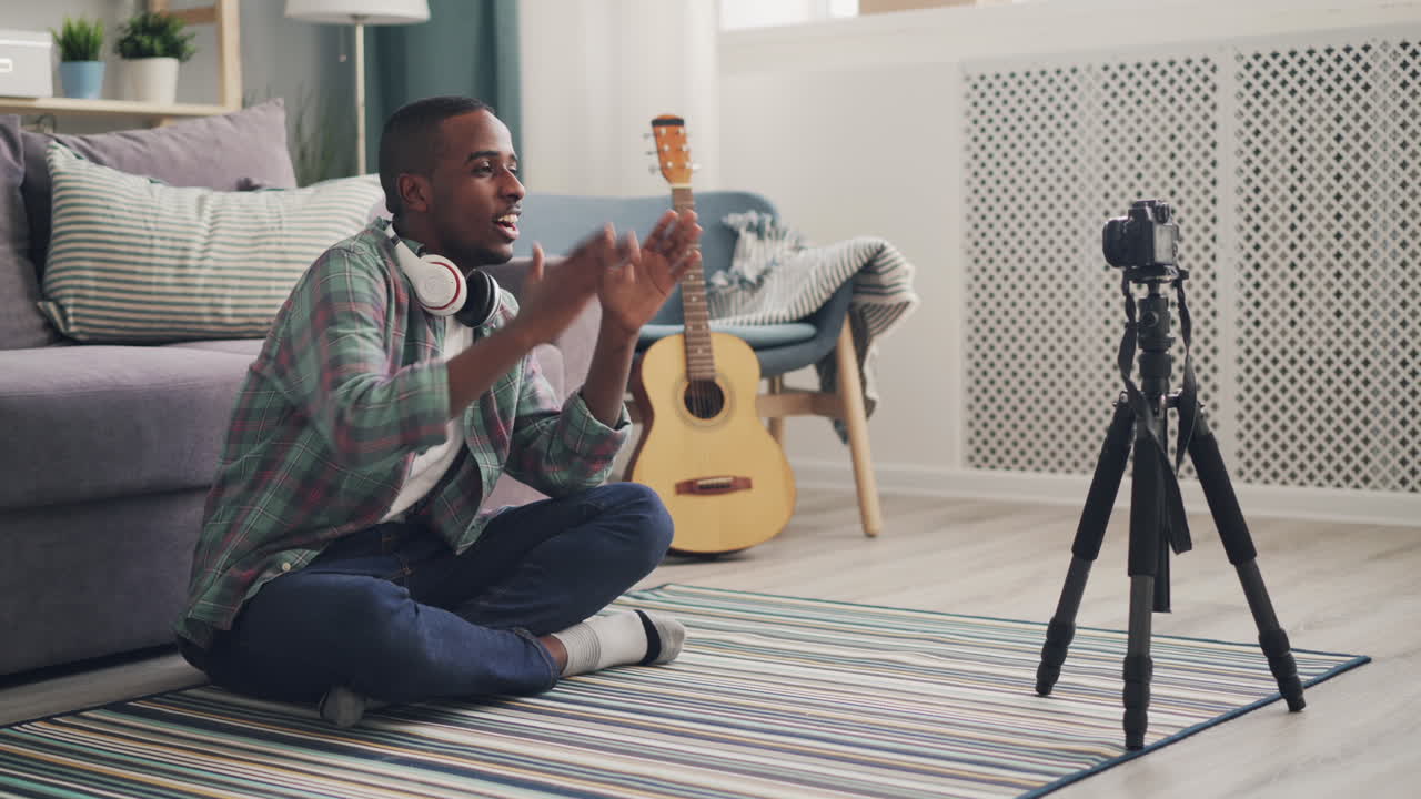 Man vlogging in living room, recording video about music and creating online content.