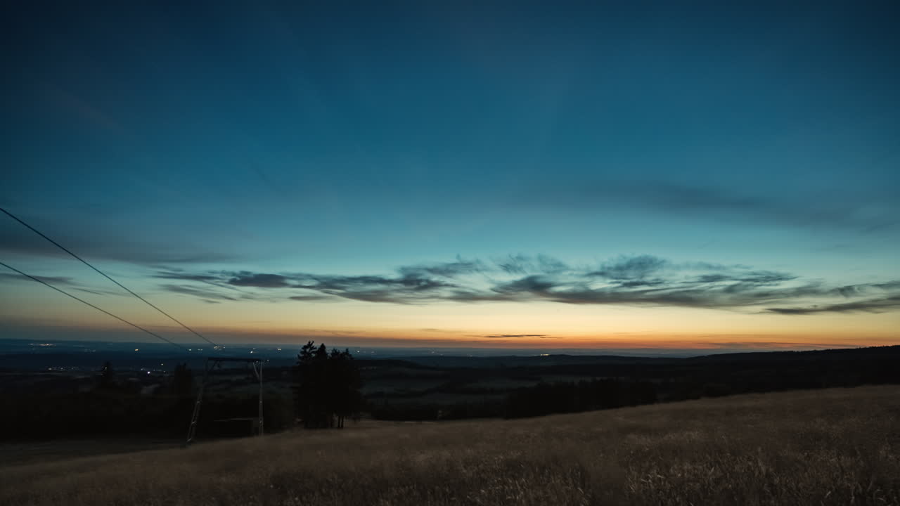 vista de lapso de tiempo de día a noche desde la cima de una colina que revela las luces de la ciudad y un cielo nocturno lleno de estrellas