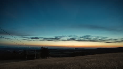 Vista-De-Lapso-De-Tiempo-De-Día-A-Noche-Desde-La-Cima-De-Una-Colina-Que-Revela-Las-Luces-De-La-Ciudad-Y-Un-Cielo-Nocturno-Lleno-De-Estrellas