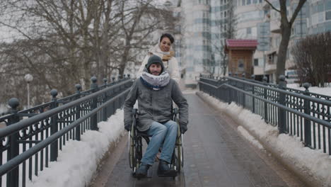 front view of a muslim woman taking her disabled friend in wheelchair on a walk in city in winter